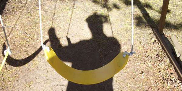 A man's shadow over a swing set