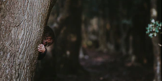 A child hides behind a tree