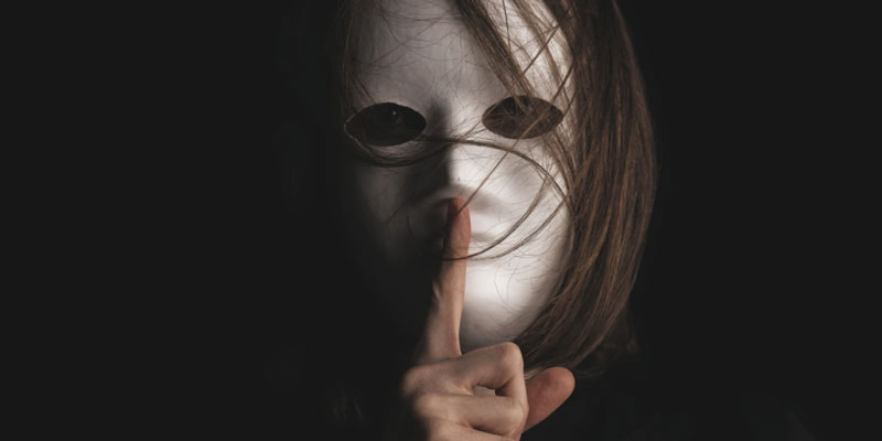 A masked figure shushes silence