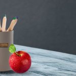 A Christian mug with colored pencils and an apple
