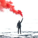 A man holds a red smoke signal on ice