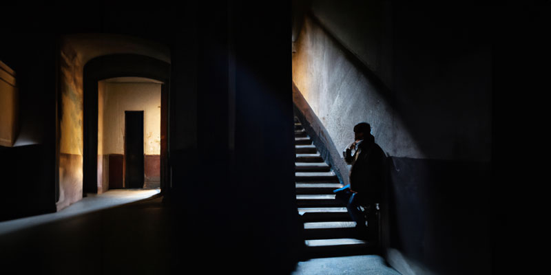 A young figure looks up the stairs in a shadowy building